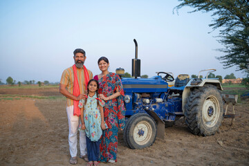 Indian farmer standing near tractor with wife and little daughter. Indian rural family.