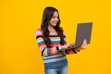 Excited face. Smart little boy with laptop in casual clothes isolated over yellow background. Happy...