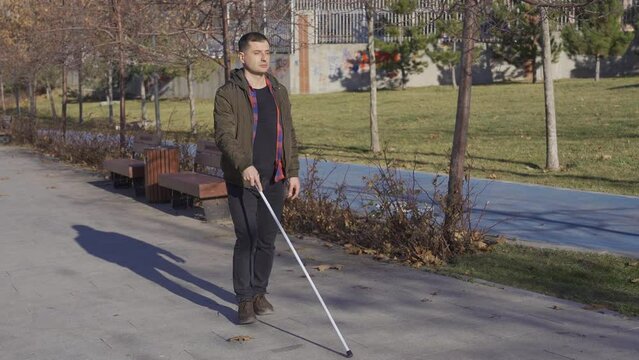 The blind man walks alone on the road. He has a walking stick.
In autumn, the blind man in the coat is walking on the road with the help of his cane.
