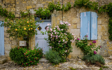 Fototapeta na wymiar Quaint and flowery facades of townhouses with colorful wooden shutters and doors in the village of Terraube in the South of France (Gers)