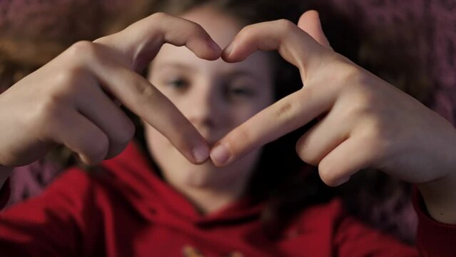 Cute little girl making a heart with her hands and smiling. Young beautiful teenager girl smiling in love showing heart symbol and shape with hands. Romantic concept.