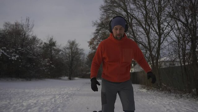 Wrong outfit and footwear for running on slippery surfaces in winter. Man jogging in snow cold weather and slips. Slippery sneakers with wrong soles for trail running on ice covered paths in woods. 
