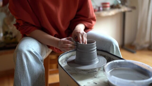 Hands of woman making earthenware jug using rotating pottery plate for subsequent exhibition of hand-made dishes. Professional master ceramist shapes product by running wet palms along walls of vessel