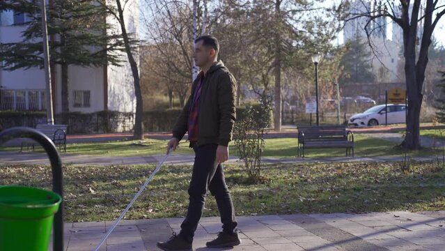 The visually impaired man is walking in the park with the help of his walking stick.
The walking of the visually impaired man in the park with the help of his cane.
