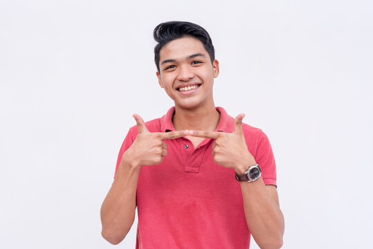 A young man makes the two fingers pointing gesture, trying to look shy. Uwu hand pose while smiling. Isolated on a white backdrop.