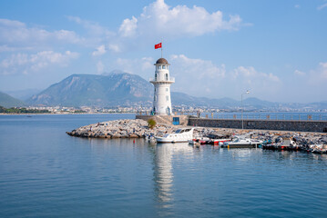 Fototapeta na wymiar Side, Turkey. October 10, 2022. Alanya lighthouse with Turkish flag at port amidst beautiful seascape with mountain and cloudy sky in the background during sunny day