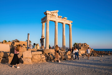 Side, Turkey. October 10, 2022. Tourists exploring old ruins of the ancient Temple of Apollo at coastline with clear blue sky in the background during sunset