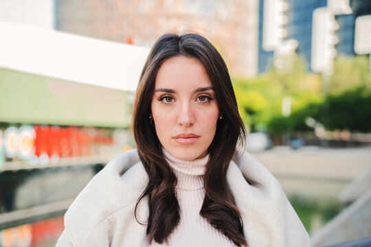 Front View Of Serious Young Woman Looking At Camera. Close Up Portrait Of Brunette Teenage Girl Standing Outdoors. Photo Of Isolated Pretty Female Lady With Sad Expression. High Quality Photo