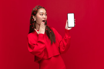 Young asian woman wearing red sweater dress show smartphone with empty screen on red background for...