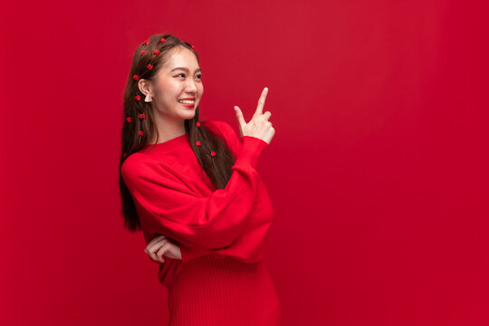 Young asian woman wearing red sweater dress with hand point to copy space on red background for happy Chinese new year and Christmas festival