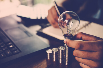 Hand businessman holding light bulb and coin stack in graph concept of creative financial planning idea and startup marketing strategy management.