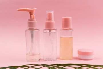 Travel concept made with bottles and jars with cosmetic products on pink background with defocused green palm leaf.