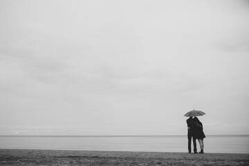 Couple together under umbrella watching sea on a date