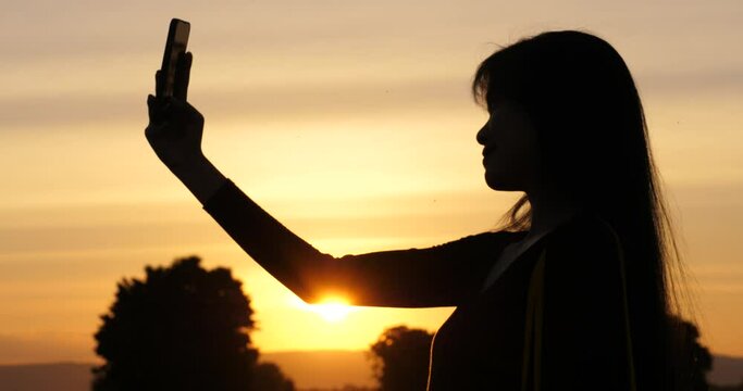 silhouette of woman using smartphone taking selfie against sunset