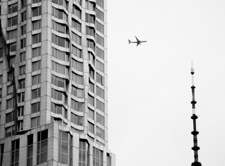 Black and white photo of an airplane flying over Manhattan buildings and city scape, USA
