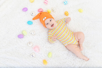 baby boy in orange clothes lying with Easter eggs, cute funny smiling little baby. The concept of...