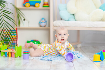 baby boy among the toys in the children's room, cute funny smiling little baby playing on the floor, the concept of children's development and games
