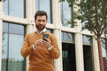 Handsome man with smartphone on city street, space for text