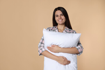Fototapeta premium Happy young woman hugging soft pillow on beige background, space for text