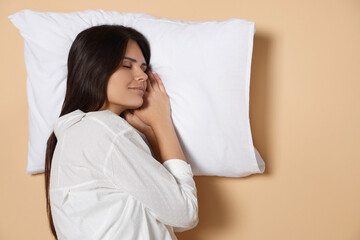 Young woman sleeping on soft pillow against beige background