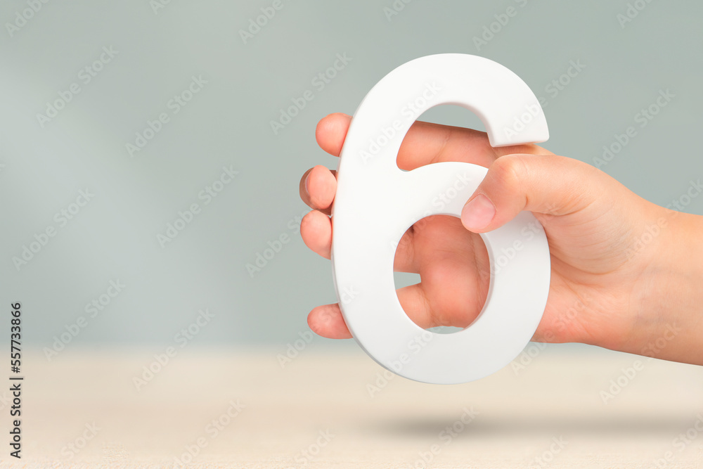 Aufkleber number six in hand. hand holding white number 6 on blurred background with copy space. concept with 