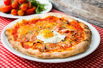Pizza with egg in the middle. Neapolitan pizza with tomato sauce, cheese and ham. Authentic Italian recipe.