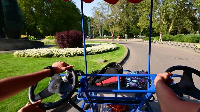 Budapest, Hungary, August 2022. Stunning POV footage from the driver's seat of a pedal quadricycle at Margaret Island. The two guys behind the wheel lead the vehicle.