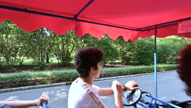 Budapest, Hungary, August 2022. Cute pov footage from the passenger seat of a pedal quadricycle. The two guys behind the wheel lead the vehicle and say hello smiling while looking into the camera.
