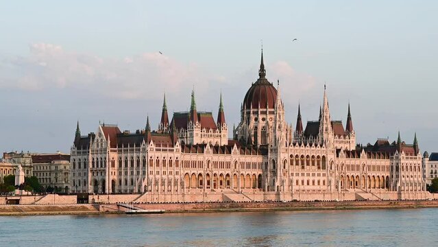 Budapest, Hungary, August 2022. Stunning three-quarter view of the parliament from the Danube river side. The yellow light of late afternoon warms the facade.