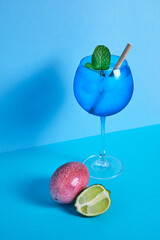 blue cocktail glass with lime, passion fruit and mint on blue minimalistic background