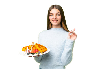 Teenager girl holding waffles over isolated chroma key background showing and lifting a finger in sign of the best