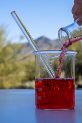 Pouring red liquid in a chemistry glass container outside