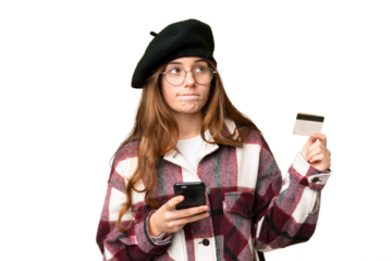 Teenager girl over isolated chroma key background buying with the mobile with a credit card while thinking