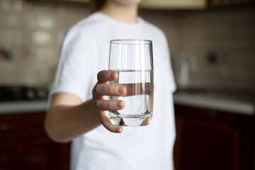 The girl holds a glass of clean water in her hand. The hand reaches forward. The concept of drinking clean water