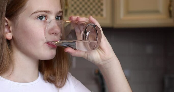 The girl drinks clean water from a glass. The concept of drinking clean water. Kitchen in the background