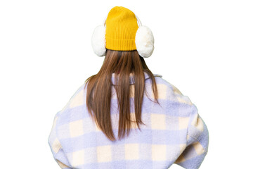 Young woman wearing winter muffs over isolated chroma key background in back position