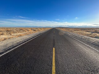 Fresh black asphalt with bright yellow markings on highway through the desert in Southern California. Blue sky overhead