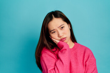 Fototapeta premium Positive young female in pink sweater looking at camera with astonished face expression while standing on blue background in studio