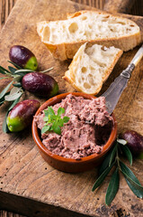 Traditional French goose pate as spread in a bowl with baguette and olives served as close-up on a rustic wooden board