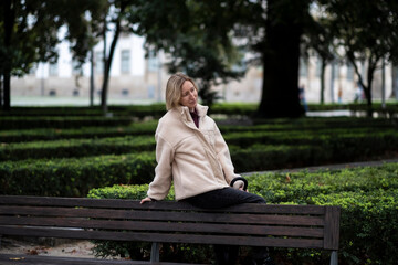 Fototapeta premium A woman sits on the back of a city park bench.