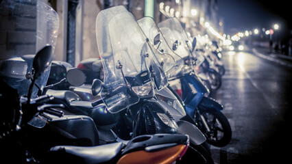 Lucca, Italy - December 2022: Scooter motorcycles parked next to each other at night on a street...