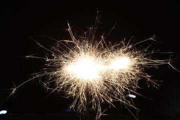 A single sparkler illuminates the darkness, its brilliant light shining like a star against the black background, the festive sparkler symbolizes joy and celebration.