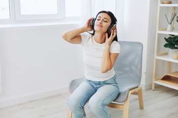 Woman listening to music on headphones sitting at home on a chair with her eyes closed, a smile and a good mood, a meditation to relieve stress