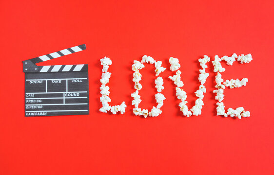 Movie clapperboard and the word love from popcorn lie on a red background.