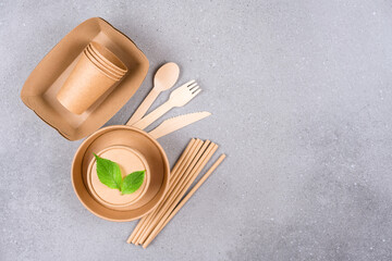 Eco paper utensils - paper plates and cups, food containers, drinking straws and wooden cutlery over gray concrete background with copy space for text. Sustainable food packaging concept