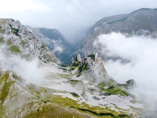 Aerial drone view of mountain in fog. Cloudy day in mountains. Cliffs and rocks at the top of mountain range. Clouds cross a mountain pass.