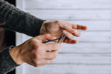 Hands of a woman, a girl close-up, making herself a manicure, cutting cuticles with special scissors on fingers, nails on a wooden white background. Close-up photography, work, beauty, art.