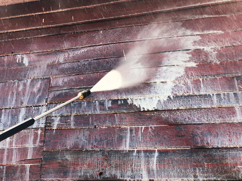 Washing with a high-pressure apparatus of a wooden red wall of a residential building from boards