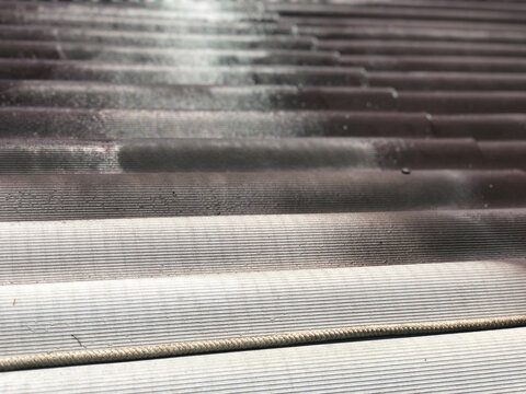 Half of the ondulin sheet on the roof of the house is painted with brown paint, illuminated by the scorching sun during the day