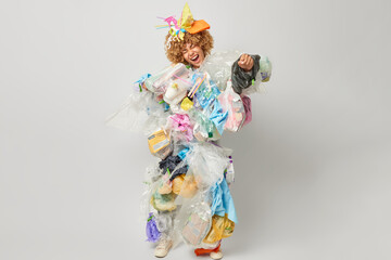 Say no to plastic. Emotional woman clenches fist exclaims loudly covered with plastic garbage busy with waste recycling collects reusable litter stands in full length isolated over grey background